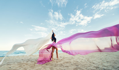 Slim Woman at the beach with long pink fabric. Sky background at the summer. Classic dancer on the...