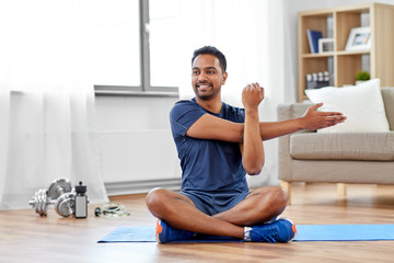 sport, fitness and healthy lifestyle concept - indian man training and stretching arm at home - Powered by Adobe