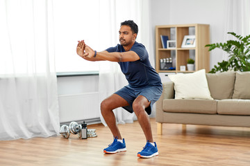 sport and healthy lifestyle concept - indian man with fitness tracker exercising and doing squats...