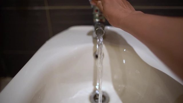 Woman testing temperature of water running from tap of bidet. Closeup view of washing basin and female hand.