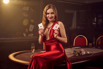 Young beautiful woman is posing against a poker table in luxury casino.