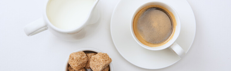 panoramic shot of coffee in cup on saucer near milk and brown sugar on white background