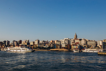 Obraz premium Scenic view of Istanbul and the Galata Tower from the Bosphorus Bay, shot on a sunny day. Vintage fishing boats on the coast in Istanbul. Passenger ferry through the Bosphorus