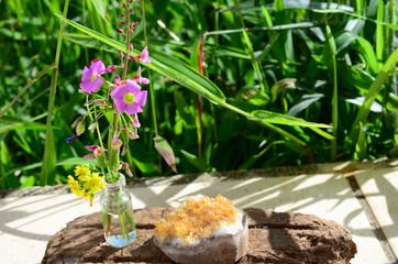 Flowers and crystals! Healing citrine crystal cluster, mini glass vase of fresh cut flowers. Nature and healing crystals shot at wood table outside. Cute witchy bohemian outdoorsy whimsical display