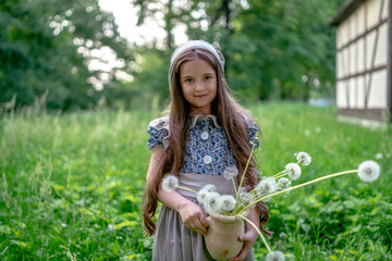 The girl in a dress in retro style with white dandelions and a clay pot amid typical architecture...