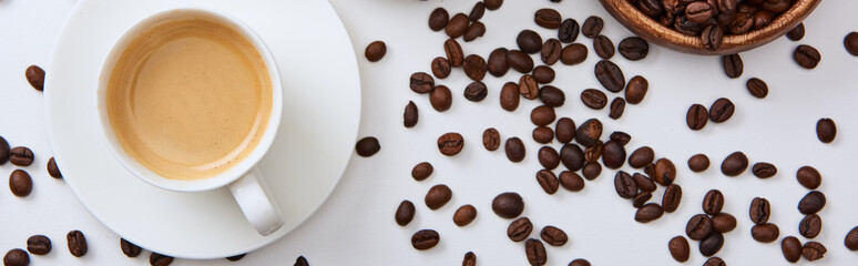 top view of coffee in cup on saucer near scattered roasted beans, panoramic shot