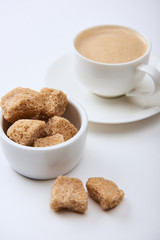 delicious coffee with foam in cup on saucer near brown sugar on white background