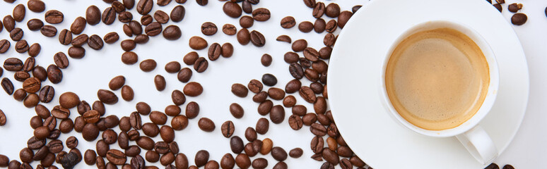 top view of coffee in cup on saucer near scattered roasted beans, panoramic shot