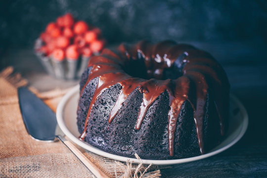 Close-up of a Devil's food bundt cake covered with melted chocolate and a bowl of fresh raspberries on a table