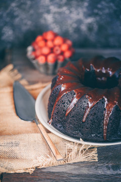 Close-up of a Devil's food bundt cake covered with melted chocolate and a bowl of fresh raspberries on a table