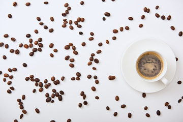 top view of delicious coffee in cup near scattered roasted beans on white background