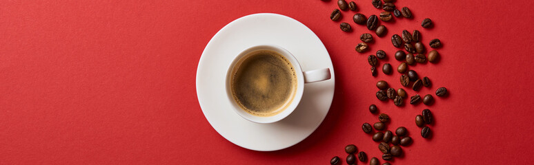 top view of delicious coffee in cup near roasted beans on red background, panoramic shot - obrazy, fototapety, plakaty