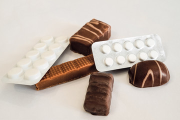 Chocolate candies and pills lie on a white table. Concept of dangerous neighborhood medicaments and sweets. Limited depth offield.