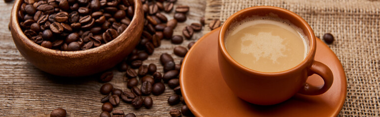 panoramic shot of coffee beans in bowl near cup of coffee on wooden background