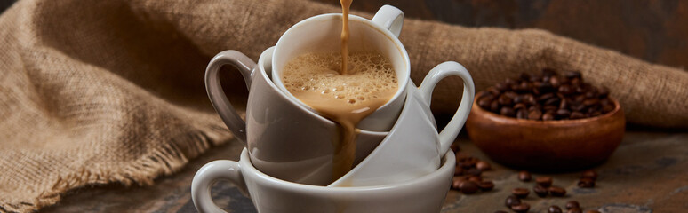 panoramic shot of flowing out hot coffee from cups near sackcloth