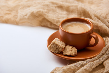 delicious coffee with foam in cup on saucer with brown sugar near cloth on white background