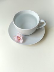 Obraz na płótnie Canvas white tea Cup in the center of white background. transparent water in a mug, a pink flower floats in the water. top view, flat layout.