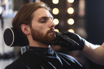 Closeup of barber shaving man beard with straight steel razor blade at barbershop. Brutal hairdresser at work