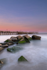 Obraz premium View on the pier in ocean from the rocky beach at sunset with long exposure