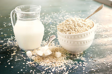 Raw Oatmeal in a bowl on the table, milk in a jug, sugar and spoons. Ingredients for Breakfast.