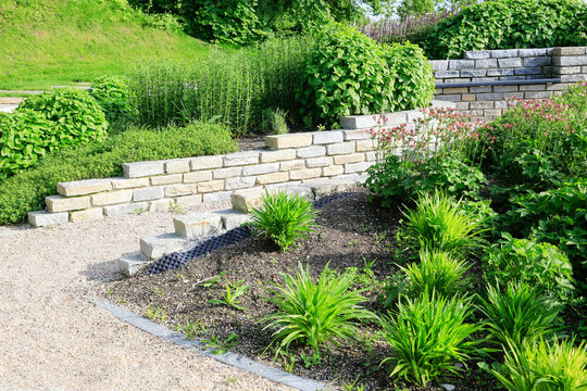 Moderner Garten- und Landschaftsbau: Gehweg und Mauern aus Natursteinen mit integrierten Sitzbänken und Anpflanzungen	