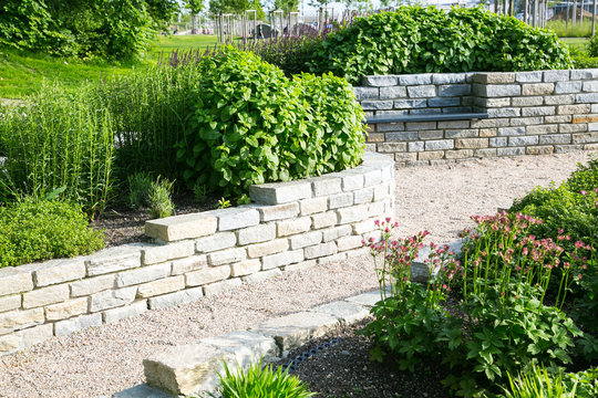 Moderner Garten- und Landschaftsbau: Gehweg und Mauern aus Natursteinen mit integrierten Sitzbänken und Anpflanzungen	