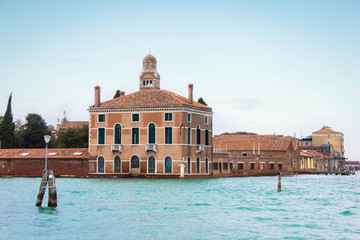 Fototapeta na wymiar Venetian lagoon and bay in the Adriatic Sea. Old architecture, red tile roof and dome. Blue water and sky. Tourism and leisure in Italy. traditional Italian architecture, a city on the water.