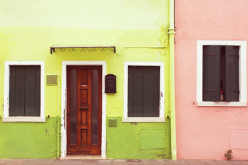 Bright green, lime and pink color painted facades of residential buildings. Old wooden entrance door and closed wooden shutter windows. Traditional colorful architecture.