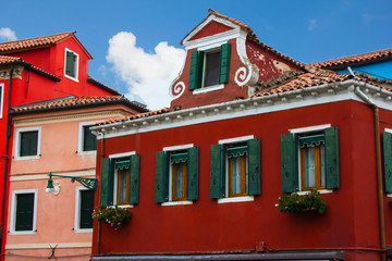 The ancient amazing burgundy facade in traditional Italian architectural style with painted loft, green wooden old shutters on the windows and blooming flowers under the windows in the pots.