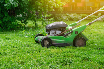 Green gasoline lawn mower on the grass in the park on the lawn