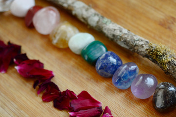 Rainbow Healing Crystals on wood table. Witches candle and fresh rose petals, rainbow stones. Clear Quartz, Pink Calcite, Jasper, Calcite, Malachite, Green Quartz, Fluorite, Sodalite, Amethyst, Onyx