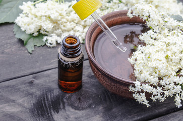 Elderberry essential oil or extract of tincture with elderberry flowers on a wooden background.