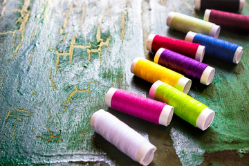 Multicolored spools of thread on wooden green decorative crackled background. Sewing accessories...