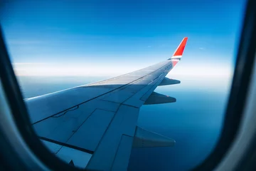 Poster aircraft wing in the sunset light. Airplane wing against the blue sky from the porthole. view from the airplane porthole to the clouds. © Stanislav