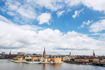 Fototapeta na wymiar Scenic summer panorama of the Old Town (Gamla Stan) architecture in Stockholm, Sweden. view from Monteliusvagen hill on island Riddarholm and tower of church. Lake Malaren with blue sky, white clouds.