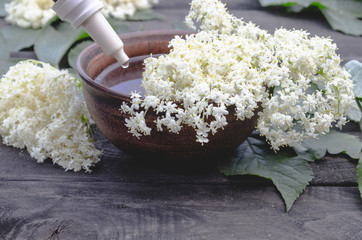Elderberry essential oil or extract of tincture with elderberry flowers on a wooden background.