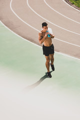 Obraz premium mixed race sportsman holding towel and sport bottle at stadium
