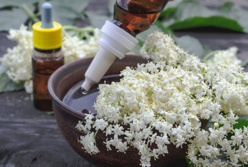 Elderberry essential oil or extract of tincture with elderberry flowers on a wooden background.