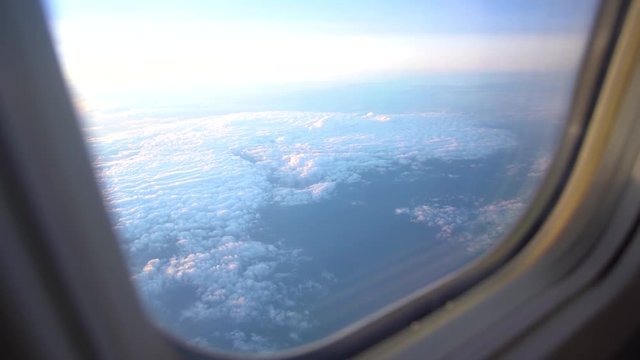Beautiful early morning sunrise sky as seen through window of airplane during flight. Real time 4k video footage of suny white and blue sky with soft delicate clouds.