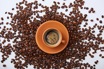 top view of coffee in brown cup on saucer near scattered roasted beans
