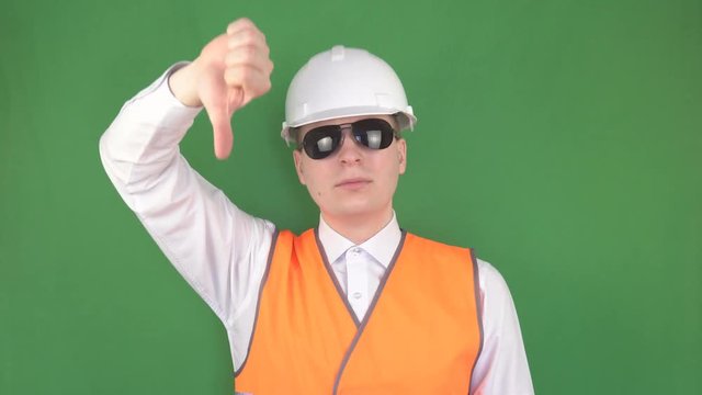 The head specialist in black glasses at the construction site shows the gestures of the team to the crane operator in the crane, green background, hromakey, safety engineering, slinger