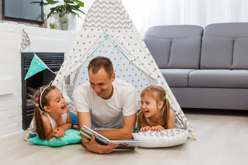 father and daughter lying on floor inside of teepee and reading book together at home