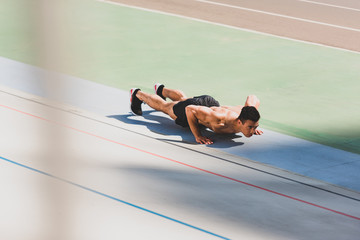 shirtless mixed race sportsman doing push ups at stadium