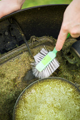 Close up view of man hand brushing off layer of wet grass stuck under automated lawnmower,...