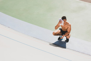 Fototapeta premium overhead view of mixed race sportsman sitting at stadium and wiping face with towel