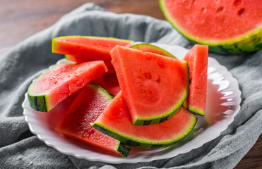 Cut slices of juicy watermelon on white plate on wooden table background