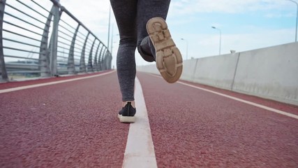 Legs of unrecognizable female athlete running on bike lane on bridge road in slow motion, back view follow shot