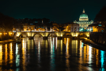 A night cityscape in Rome, Italy featuring an arch bridge and Saint Peter’s Basilica.