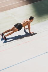 mixed race sportsman standing in plank at stadium