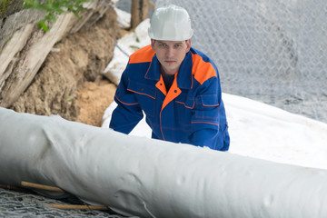 a worker in overalls covers stones and iron mesh with white wrap